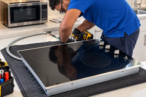 Technician working on a removed glass cooktop on a padded kitchen counter