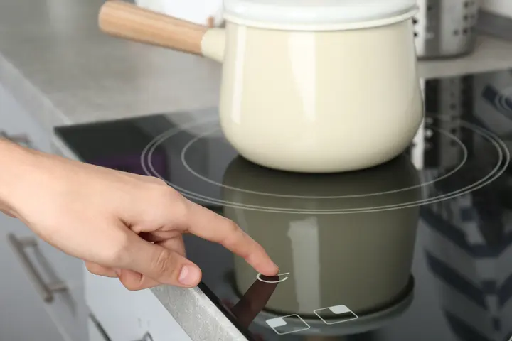 Person pressing a glass cooktop touch control with a saucepan on a cooking zone