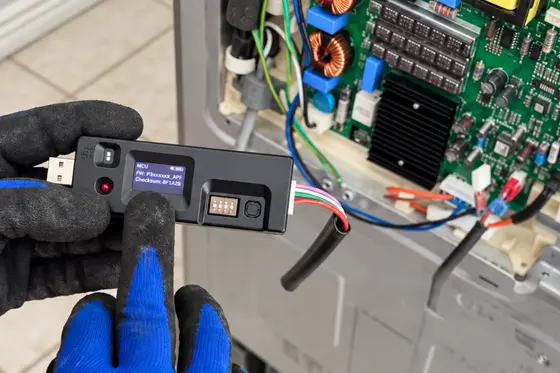 Technician holding an LG update jig beside a refrigerator control board