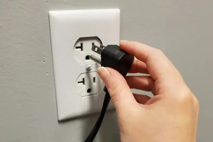 Hand unplugging a power cord from a wall outlet before refrigerator service